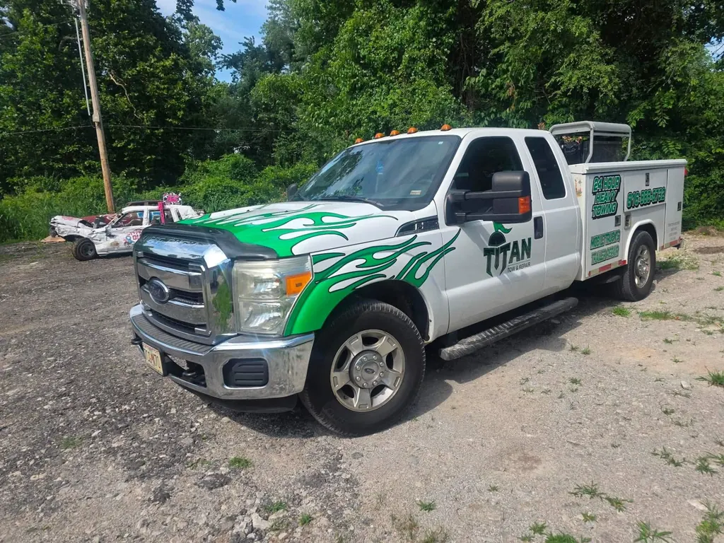 Titan Tow & Repair 24-hour heavy-duty mobile service truck — white Ford F-Series with green flame graphics, Titan Tow & Repair Spartan-helmet logo, utility body labeled '24 Hour Heavy Towing · Mobile Truck & Trailer Repair · (816) 888-8732' — parked at the Liberty, MO shop.